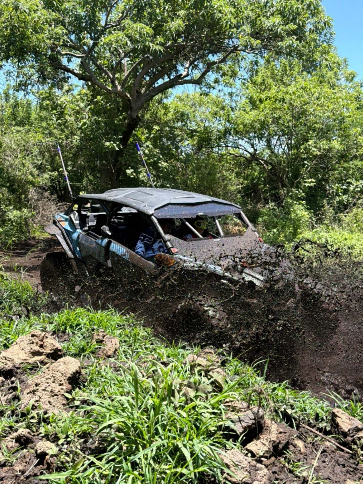 Maverick X3 atravesando un charco de lodo entre la vegetación.