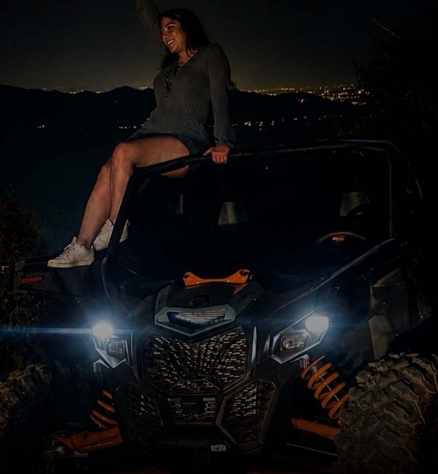 Una persona sentada sobre un Maverick X3 de noche, con las luces del valle al fondo.